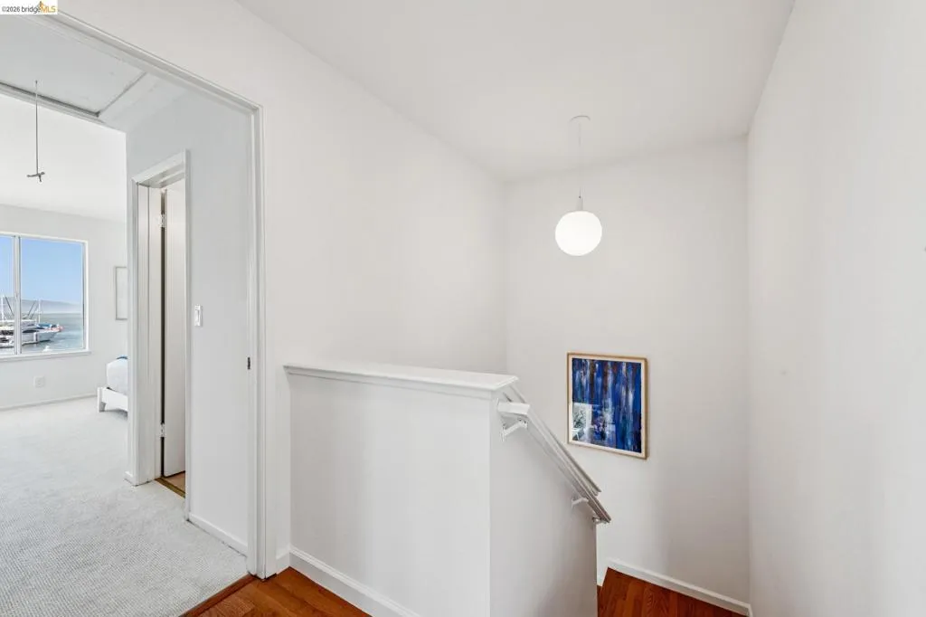 White painted walls and trim throughout, with hardwood flooring leading to a carpeted room featuring a large window with water and boat scenery