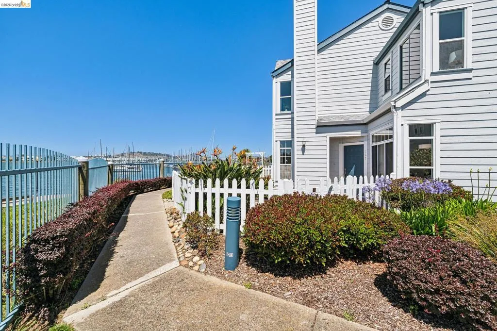 Waterfront property featuring a concrete pathway, a picket fence, and a metal security fence