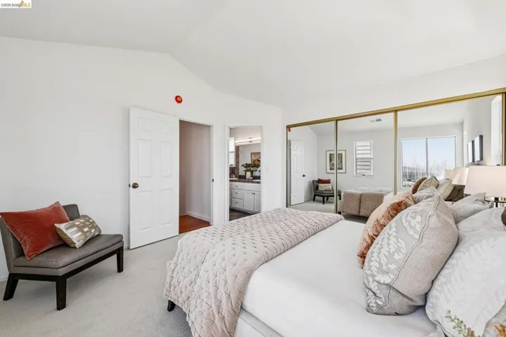 Bright bedroom featuring white walls, vaulted ceilings, and light-toned carpet