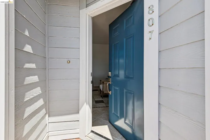 Entryway featuring a paneled teal door with polished hardware, white horizontal siding, and tiled flooring