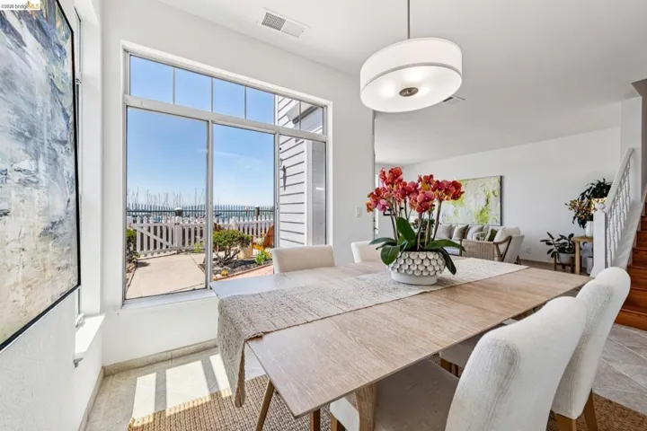 Dining area featuring a large picture window, a contemporary drum pendant light fixture, light wood-finish flooring, white painted walls, and a staircase with wood treads and white risers