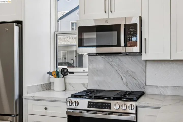 Stainless steel range and microwave oven with white shaker-style cabinetry, a white countertop, and a marble-patterned backsplash