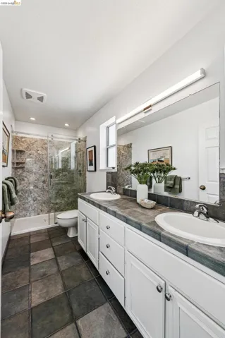 Bathroom featuring a double vanity with white cabinetry and dark tile countertop, dual undermount sinks, and a large wall-mounted mirror