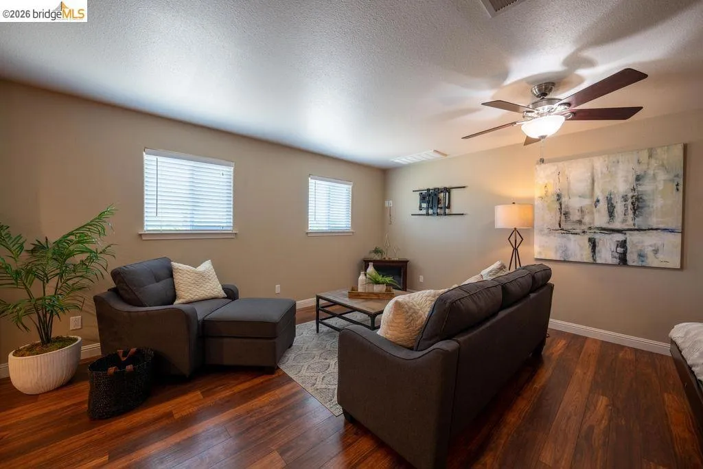 Living area featuring rich wood-finish flooring, neutral-toned walls, and a ceiling fan with integrated lighting