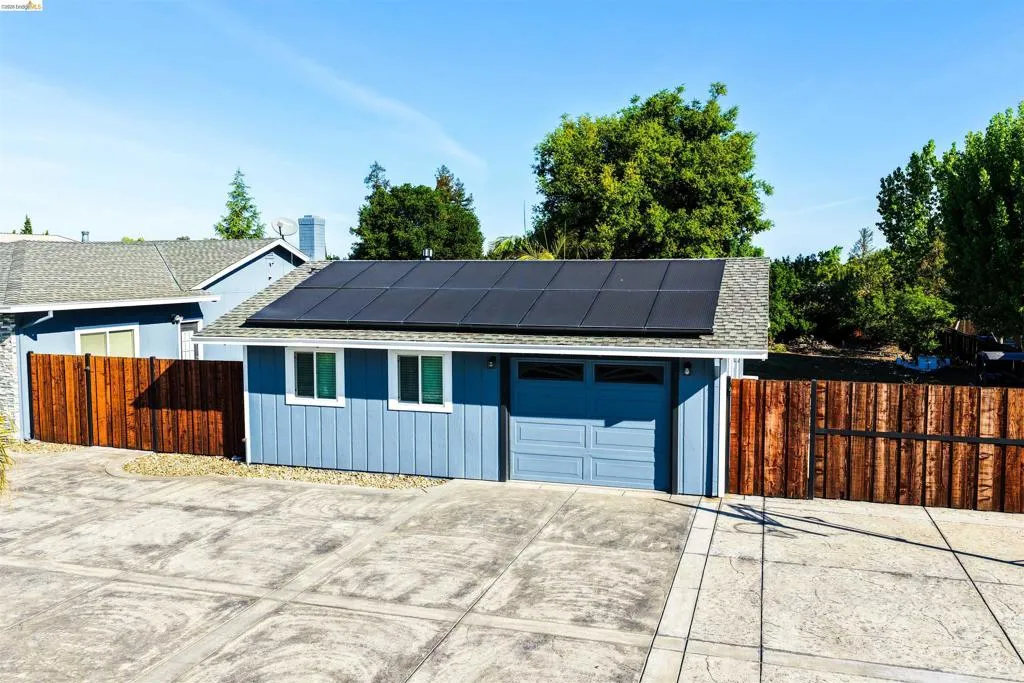 Blue exterior with white trim, featuring solar panels on the roof, an attached garage, and a wood privacy fence