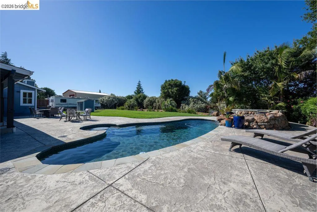 Freeform swimming pool featuring an integrated spa with stone surround, complemented by a stamped concrete patio and a manicured lawn