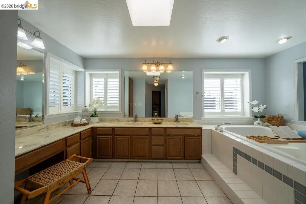 Spacious bathroom featuring a built-in soaking tub, dual vanity with undermount sinks, wood cabinetry, and plantation shutters