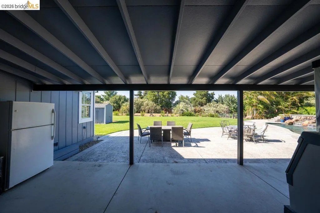 Expansive covered patio with exposed beam ceiling, concrete flooring, and direct access to an extensive lawn
