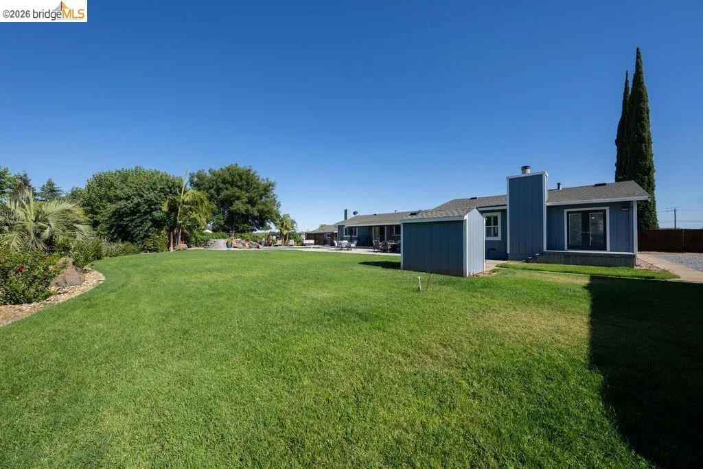 Expansive lawn area with a blue exterior building, a separate storage shed, and a paved driveway