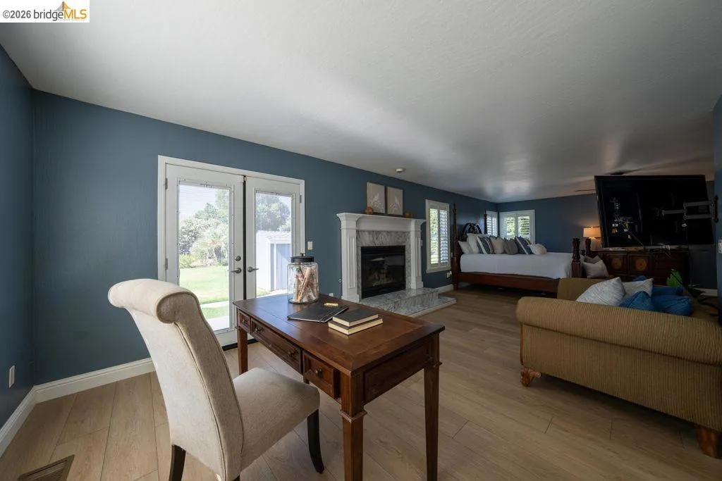 Spacious interior featuring wood-finish flooring, a white mantel fireplace with a stone surround, and plantation shutters