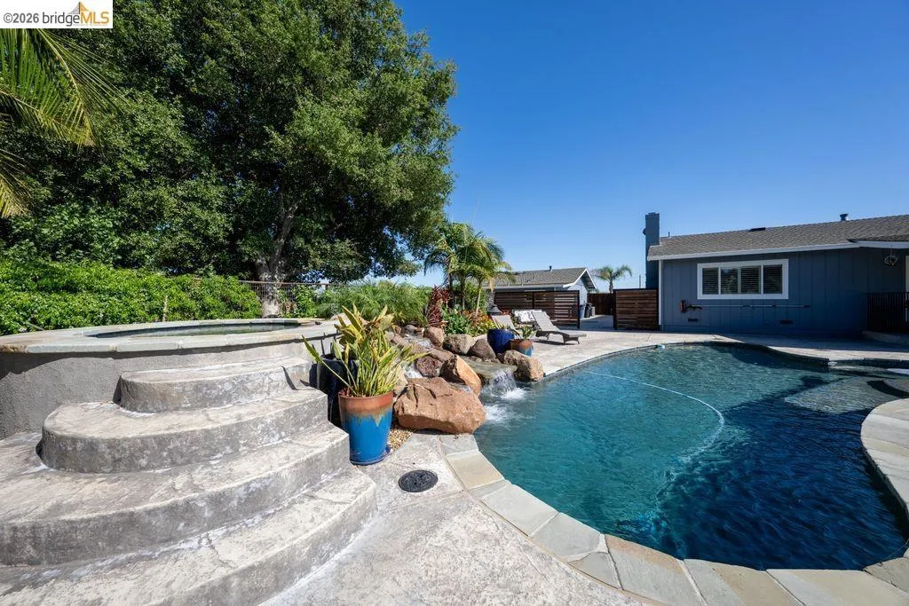 Curved swimming pool featuring a waterfall, integrated spa with stone steps, and flagstone coping