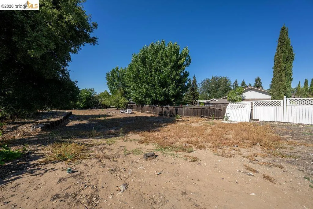 Open lot featuring a partial white lattice fence and a darker wood fence