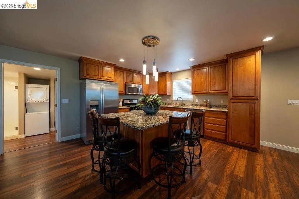 Kitchen featuring a central island with a granite countertop, wood-finish flooring, recessed lighting, and stainless steel appliances