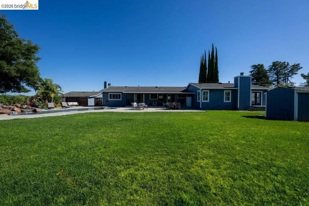 Expansive green lawn with a swimming pool, rock water feature, and a blue single-story residence
