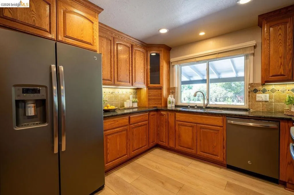 Corner kitchen featuring wood-finish cabinetry, dark countertops, and a tiled backsplash