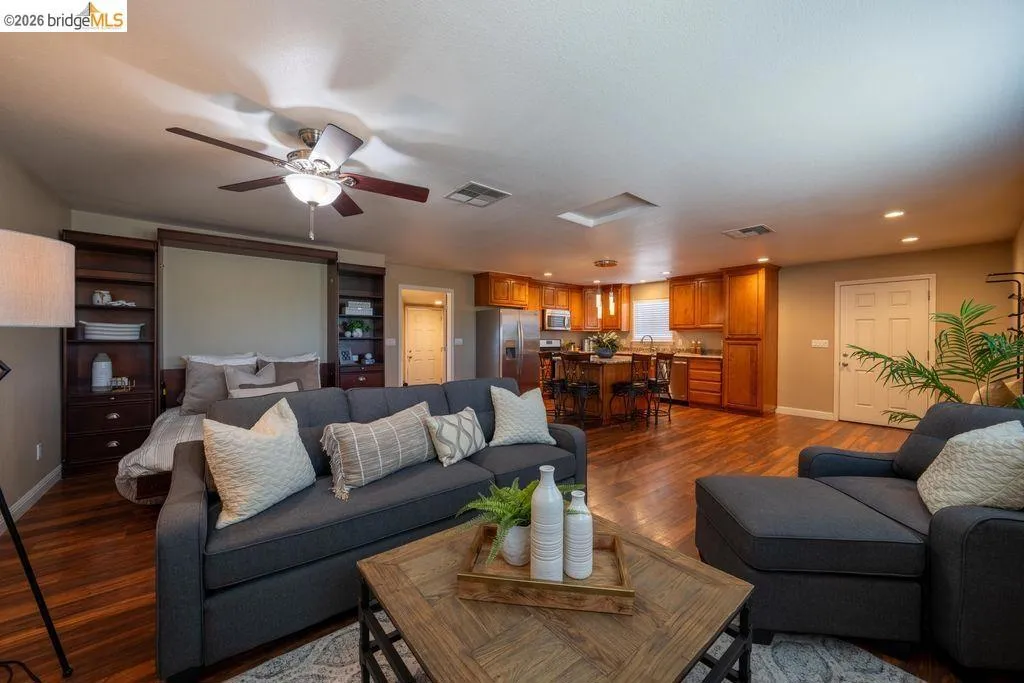 Open-concept living area featuring wood-finish flooring, a built-in wall bed system, a ceiling fan with integrated lighting, recessed lighting, and a kitchen with wood cabinetry