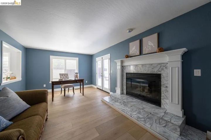 Living area featuring a fireplace with a white mantel and multi-toned stone surround, wood-finish flooring, white plantation shutters, and French doors