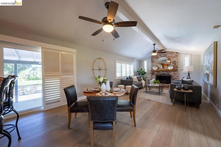 Open-concept living space featuring wood-finish flooring, a brick fireplace with a wood mantle, and exposed beam ceilings