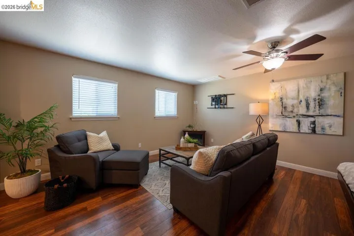 Living area featuring rich wood-finish flooring, neutral-toned walls, and a ceiling fan with integrated lighting