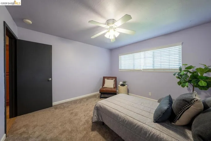 Bedroom featuring a ceiling fan with integrated lighting, a horizontal window with blinds, light purple wall paint, and gray carpet flooring