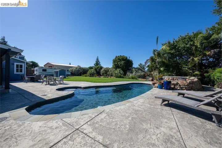 Freeform swimming pool featuring an integrated spa with stone surround, complemented by a stamped concrete patio and a manicured lawn