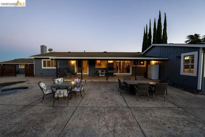 Expansive stamped concrete patio featuring a built-in pool with spa, multiple outdoor access points, and privacy fencing