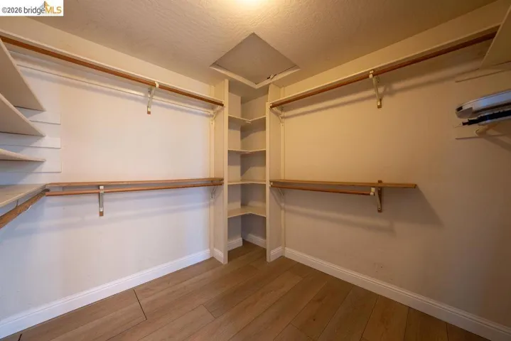 Custom closet system featuring wood-finish flooring, white baseboards, multiple hanging rods, and integrated corner shelving