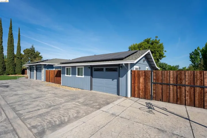 Exterior featuring two structures with light blue siding and dark gray garage doors, complemented by solar panels on the roof