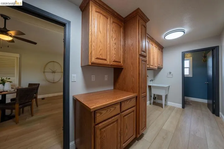 Utility area featuring light wood-finish flooring, warm wood cabinetry, a utility sink, and a flush-mount ceiling light fixture