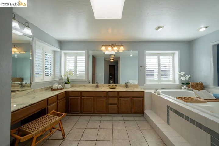 Spacious bathroom featuring a built-in soaking tub, dual vanity with undermount sinks, wood cabinetry, and plantation shutters