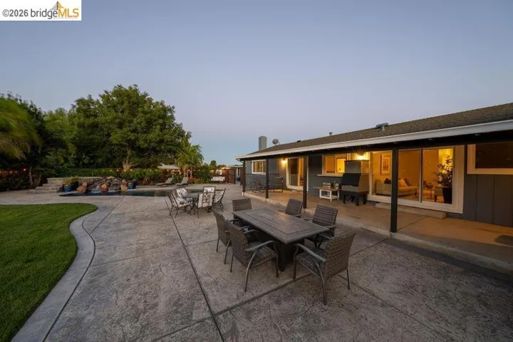 Expansive stamped concrete patio with multiple seating areas, a swimming pool with a rock waterfall feature, and a manicured lawn