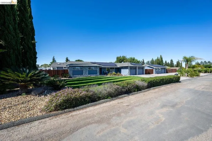 Ranch-style residence featuring a stone and siding exterior, multiple garage bays, solar panels, and a manicured front lawn