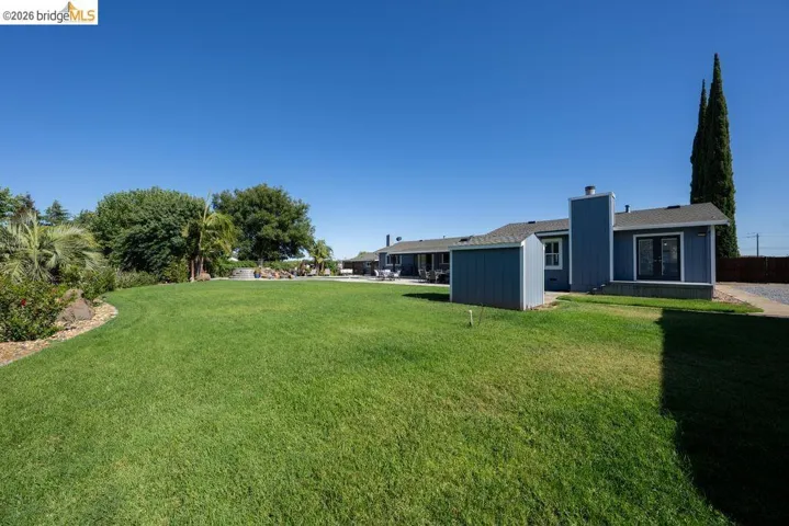 Expansive lawn area with a blue exterior building, a separate storage shed, and a paved driveway