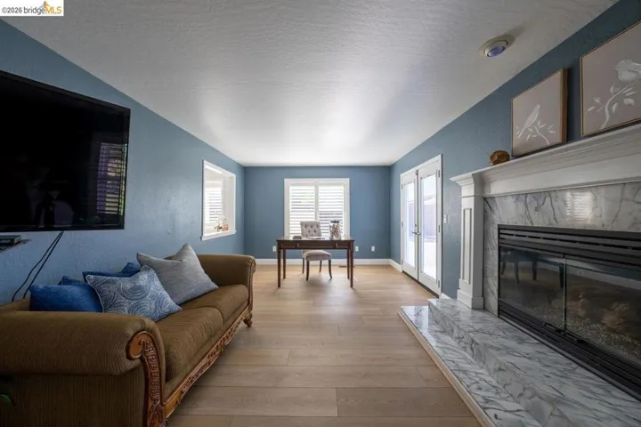 Living area with light wood-finish flooring, a fireplace featuring a white marble surround and hearth, and double French doors with white frames