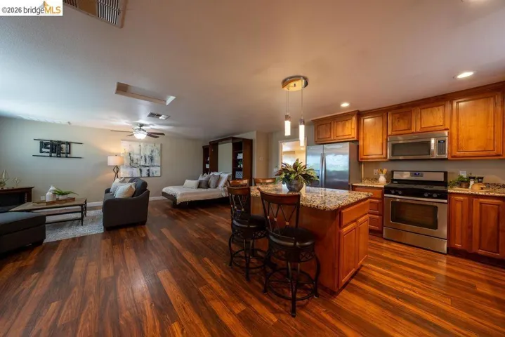 Open-concept living space featuring wood-finish flooring, a kitchen island with pendant lighting, stainless steel appliances, and wood cabinetry
