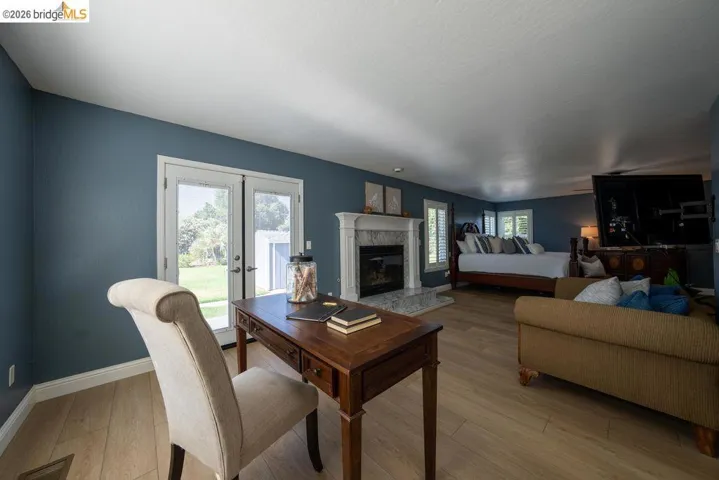 Spacious interior featuring wood-finish flooring, a white mantel fireplace with a stone surround, and plantation shutters
