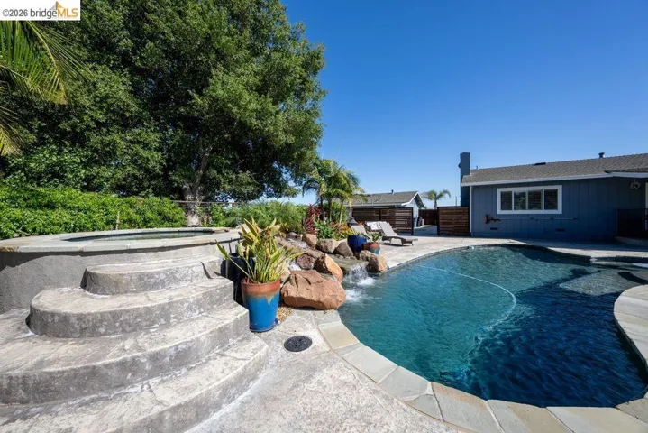 Curved swimming pool featuring a waterfall, integrated spa with stone steps, and flagstone coping