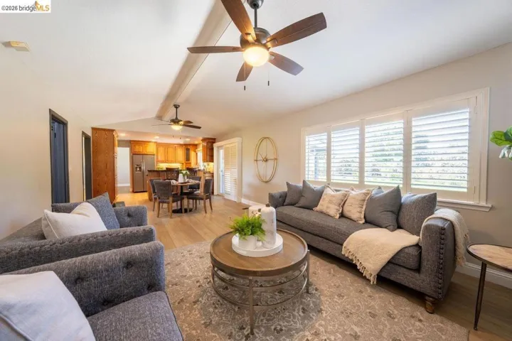 Open-concept living area with light wood-finish flooring, white walls, and vaulted ceilings featuring exposed beams