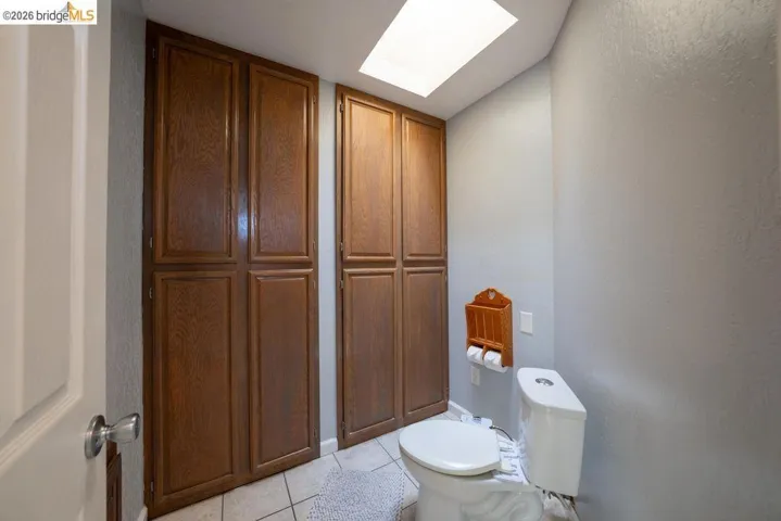 Bathroom featuring two tall built-in wood-finish storage cabinets, a skylight, ceramic tile flooring, and a white toilet