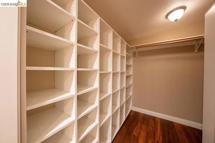 Custom built-in shelving system featuring adjustable white shelves, a dedicated hanging rod, rich wood-finish flooring, white baseboards, and an overhead flush-mount light fixture