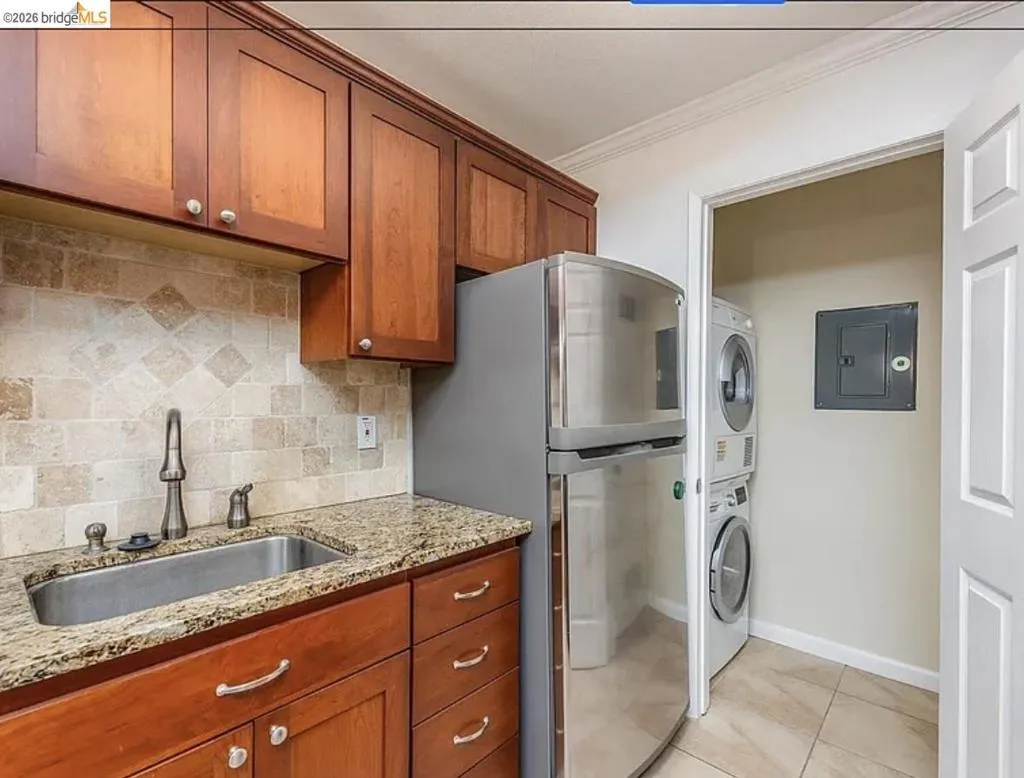 Kitchenette featuring wood cabinetry, granite-style countertops, stainless steel sink, and a tiled backsplash
