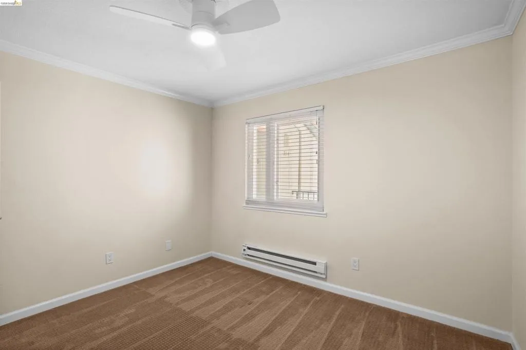 Neutral-toned room featuring a white ceiling fan with integrated lighting, a single window with blinds, baseboard heating, and light brown patterned carpeting