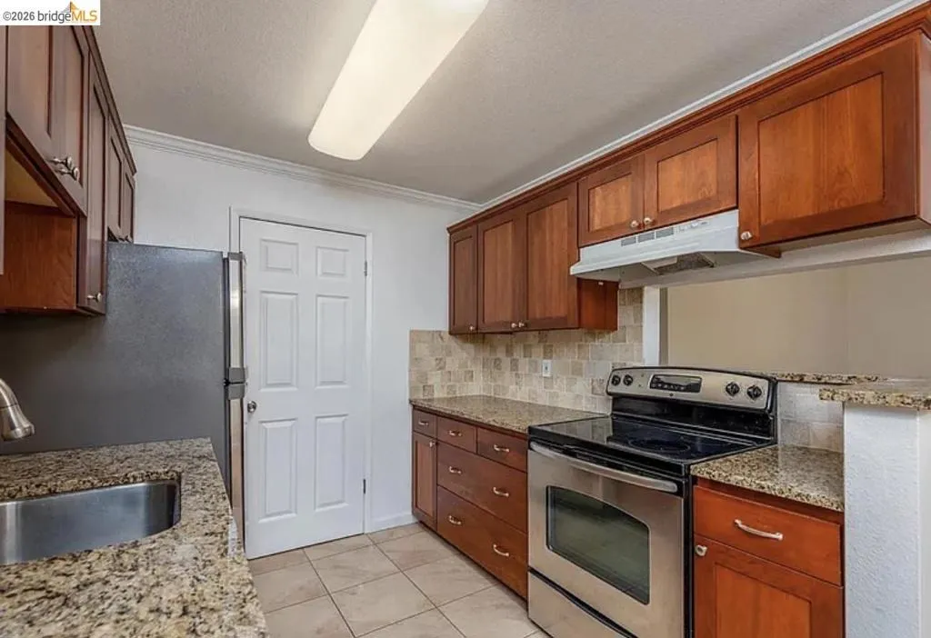 Kitchen featuring wood cabinetry, granite countertops, a stainless steel sink, and tile flooring