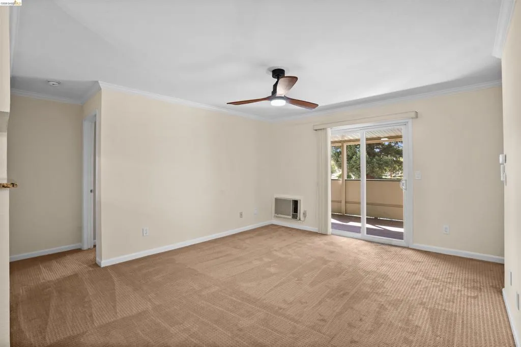 Carpeted interior space featuring a ceiling fan with integrated lighting, crown molding, and an in-wall air conditioning unit