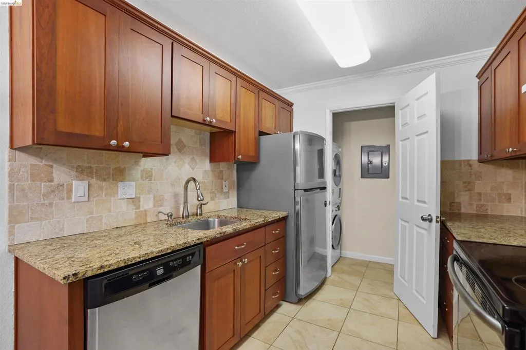 Kitchen featuring granite countertops, wood-finish cabinetry, stainless steel dishwasher, and a tile backsplash