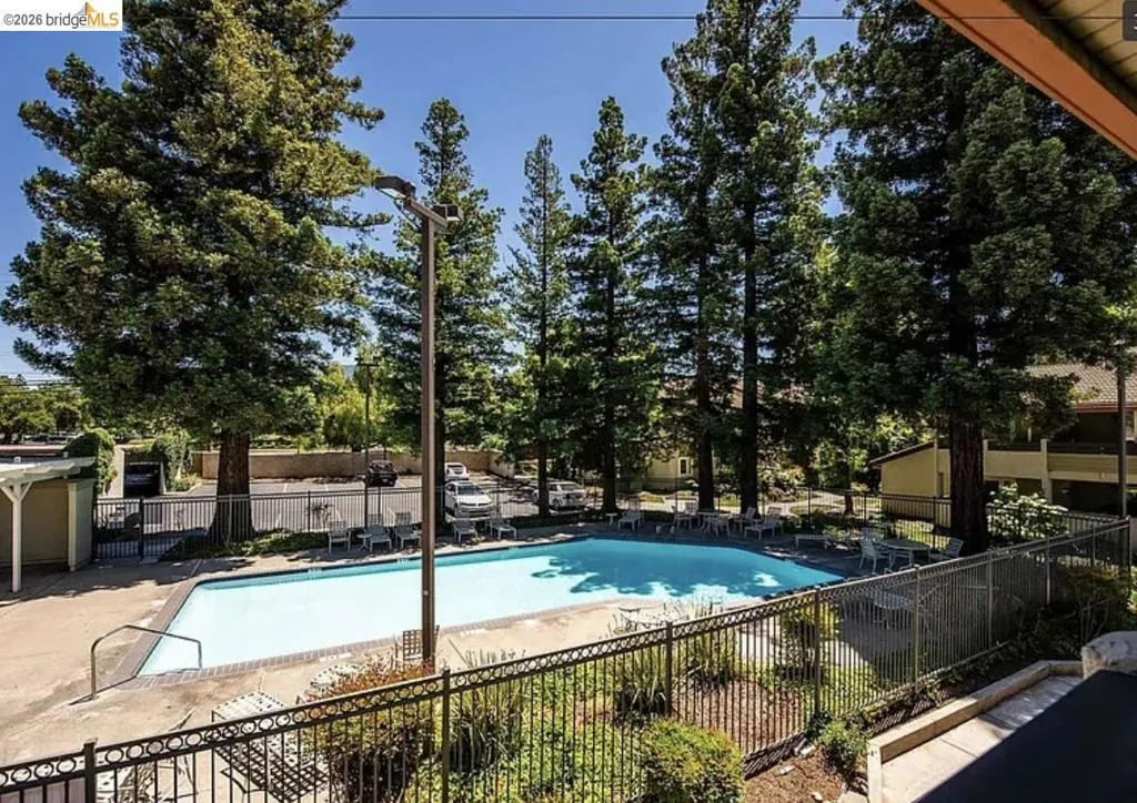 Outdoor swimming pool area featuring a metal perimeter fence, surrounding concrete decking, and multiple lounge chairs