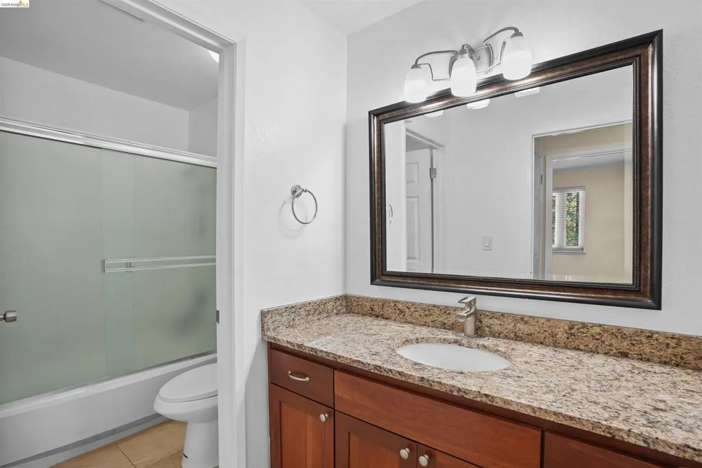 Bathroom featuring a single vanity with a granite-style countertop, wood-finish cabinetry, and a framed mirror with a three-light fixture