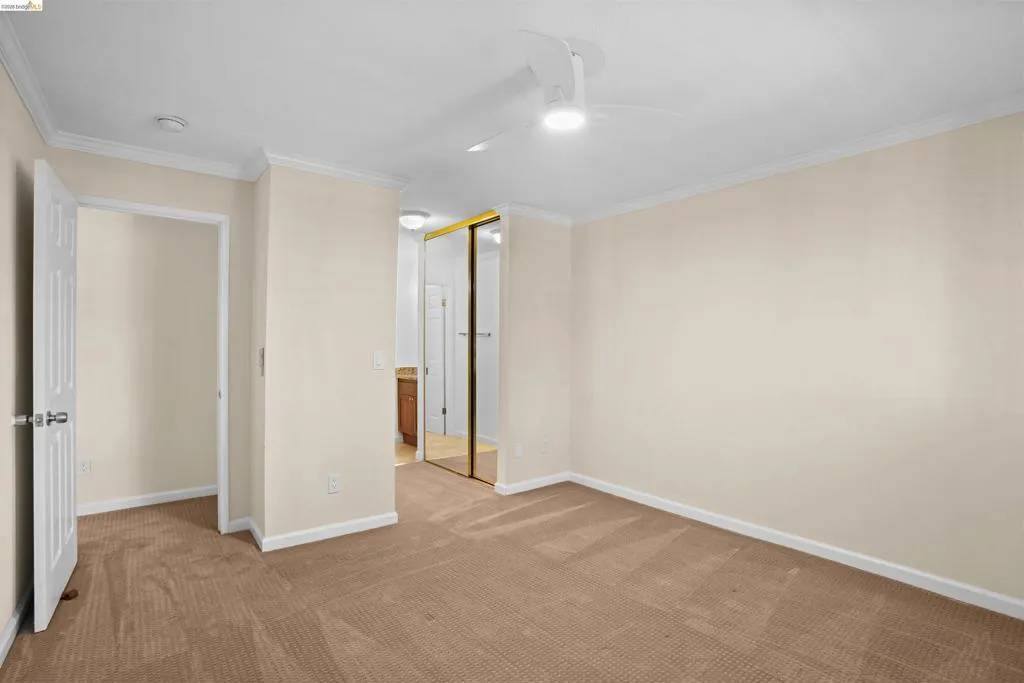 Carpeted room featuring a ceiling fan with integrated lighting, crown molding, and a partial view of a bathroom vanity with a wood-finish cabinet and mirror