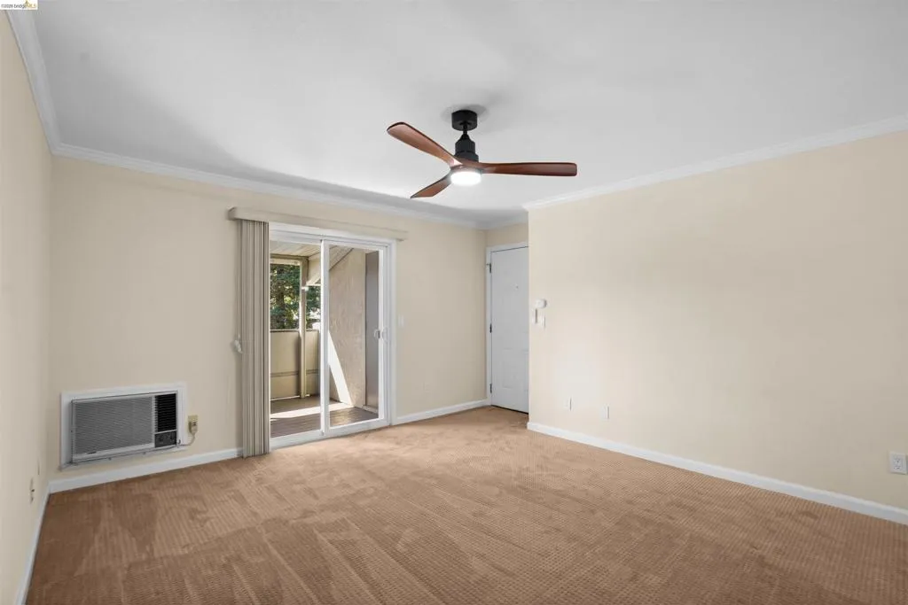 Carpeted interior space featuring a ceiling fan with integrated lighting, crown molding, and a sliding glass door leading to an exterior balcony