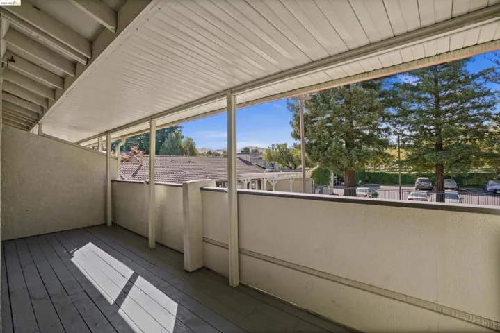 Covered balcony featuring wood-finish flooring, stucco walls, and a slatted ceiling